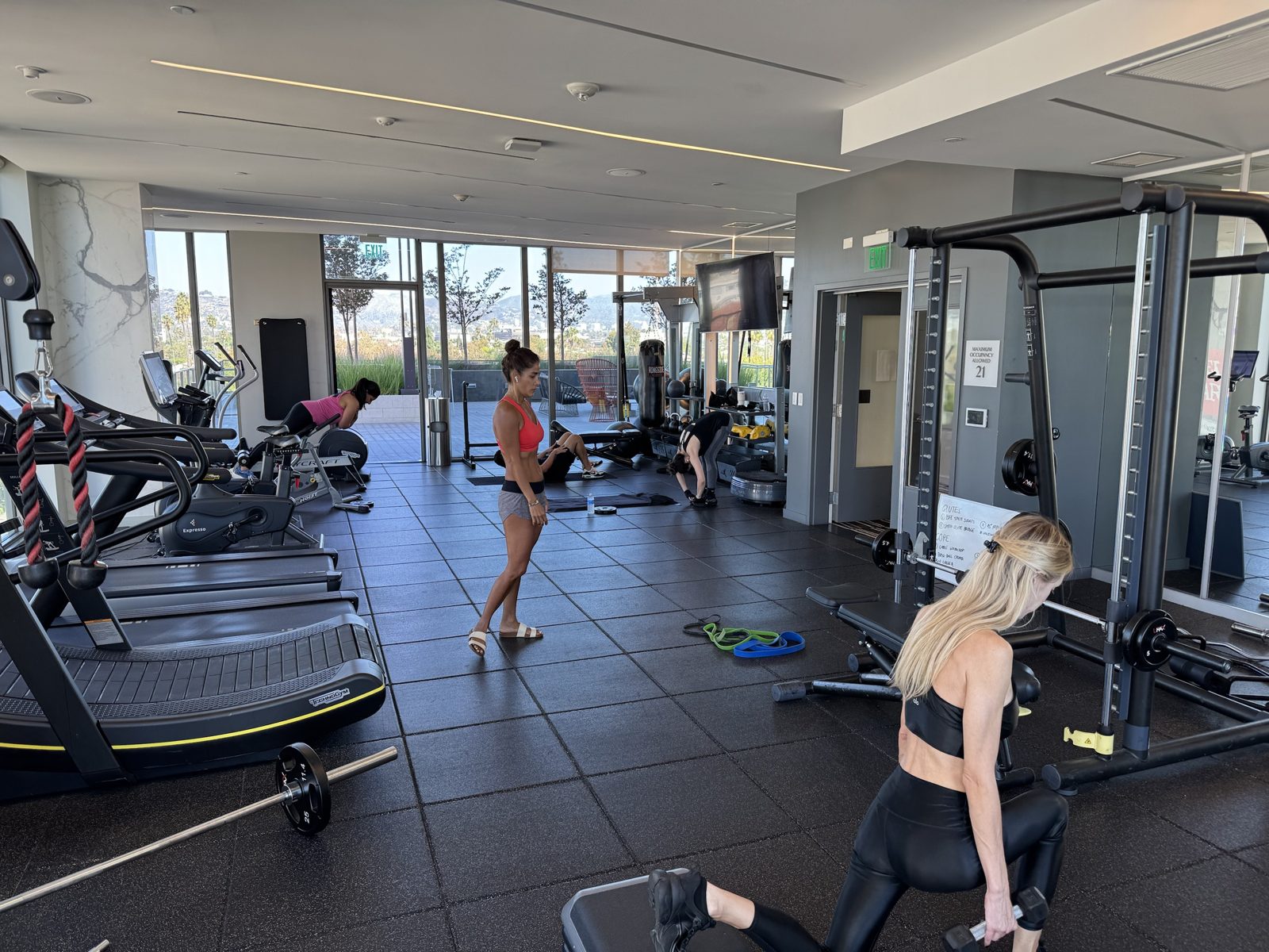 Residents training in the gym at Vision on Wilshire, one doing a split squat with dumbbells while others stretch and use the equipment